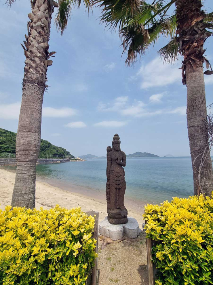 Statue, flowers and palm trees in front of a beach near Fukuoka